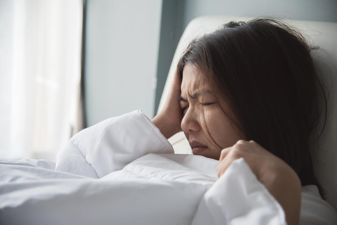 Woman with migraine in bed holding right side of head.