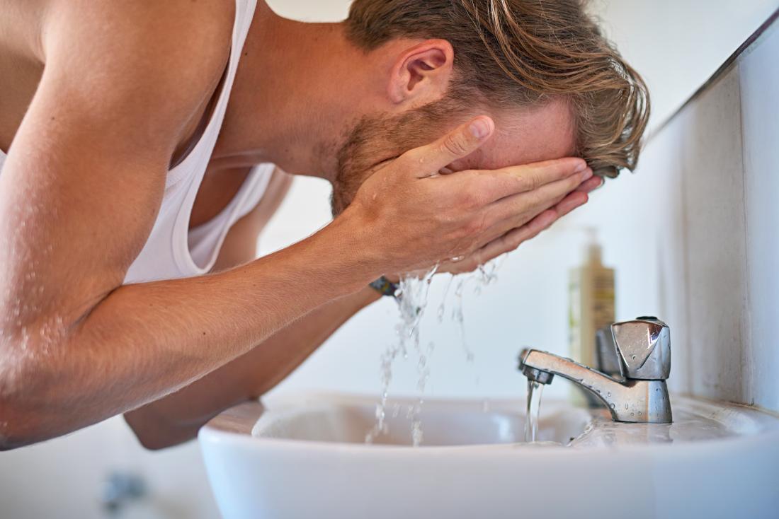 Man washing his face in bathroom sink.