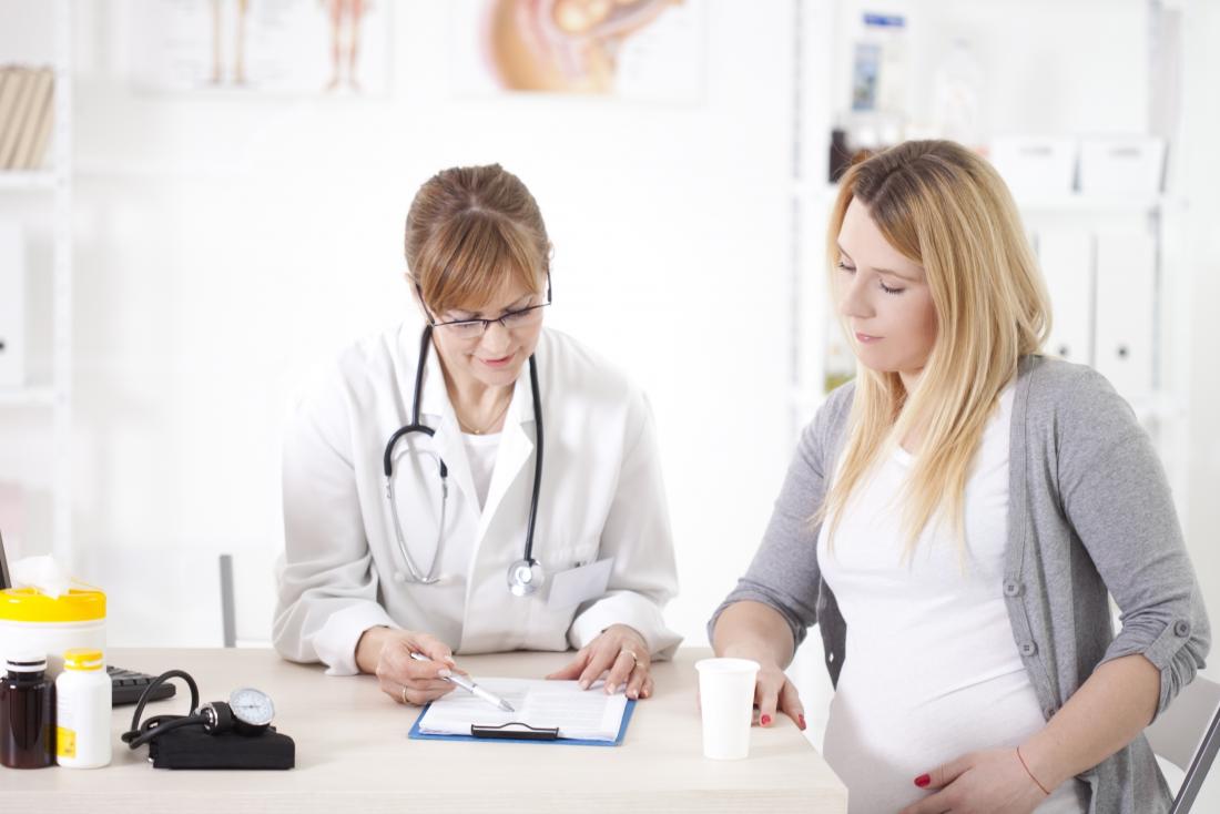 Pregnant woman in consultation with female doctor looking at clipboard of notes in office.
