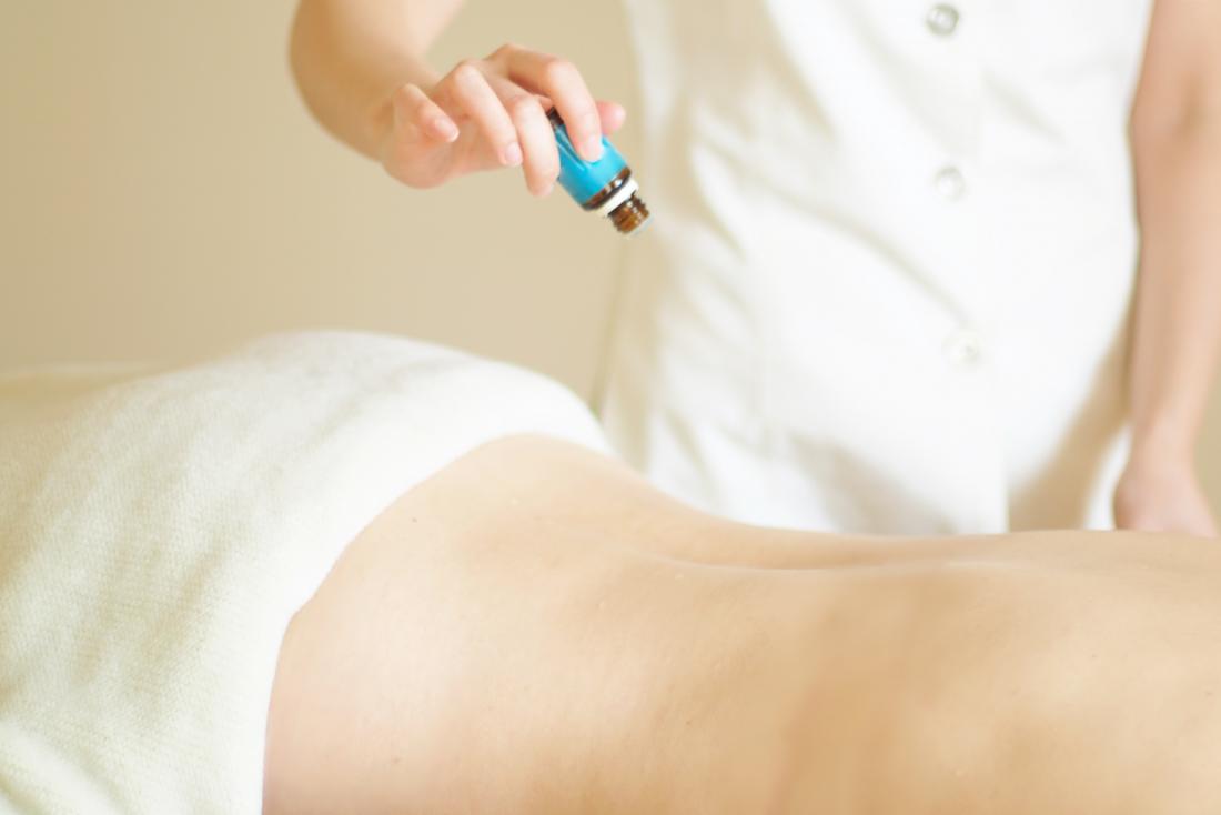 Essential oil being poured from bottle on person back during massage therapy and aromatherapy.