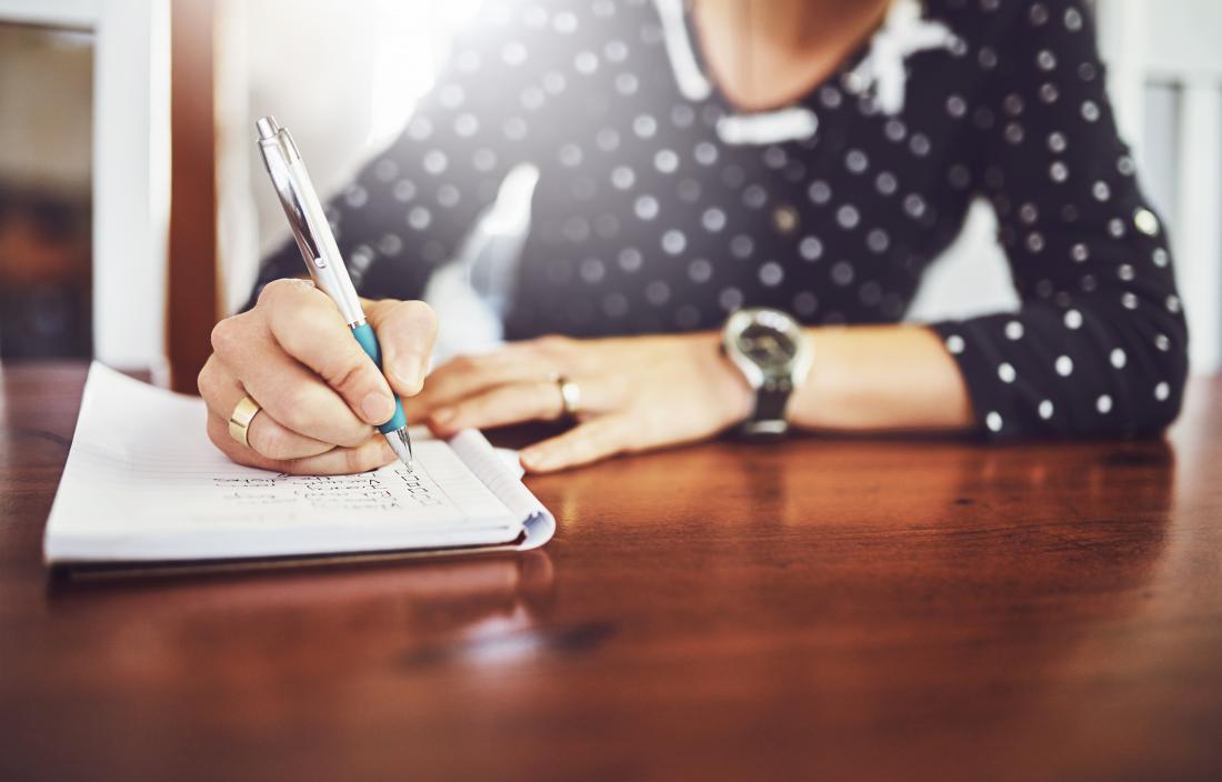 Person writing notes in notepad diary or journal book on table.