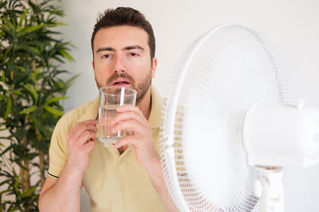 man drinking glass of water in front of electric fan