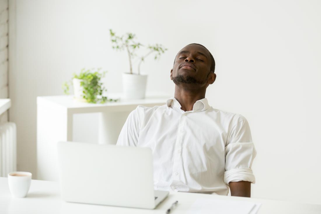 Man sitting at desk in minimalist office, doing deep breathing exercises.