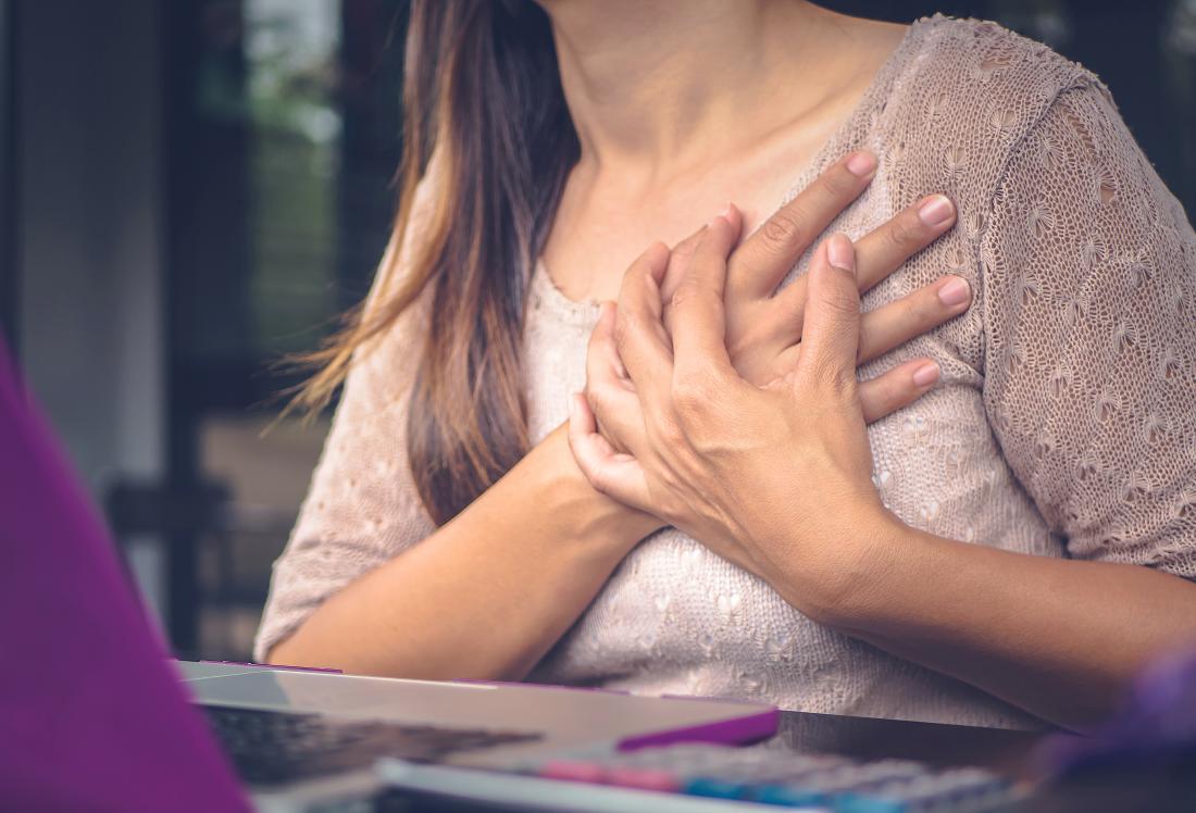 Woman with chest pains clutching her chest while sitting at desk.
