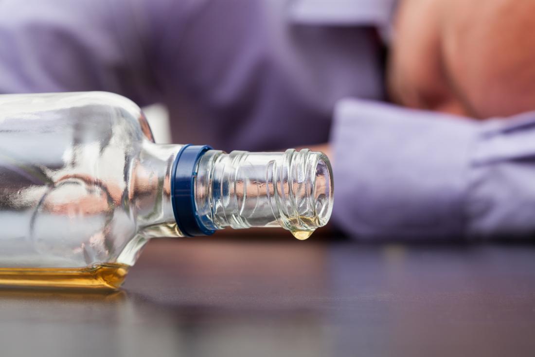 bottle of alcohol on its side with man slumped on table
