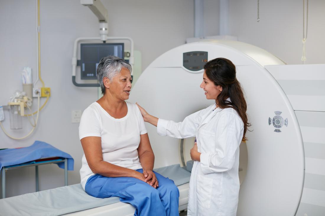 Mature woman sitting on CT scan machine about to have image test.