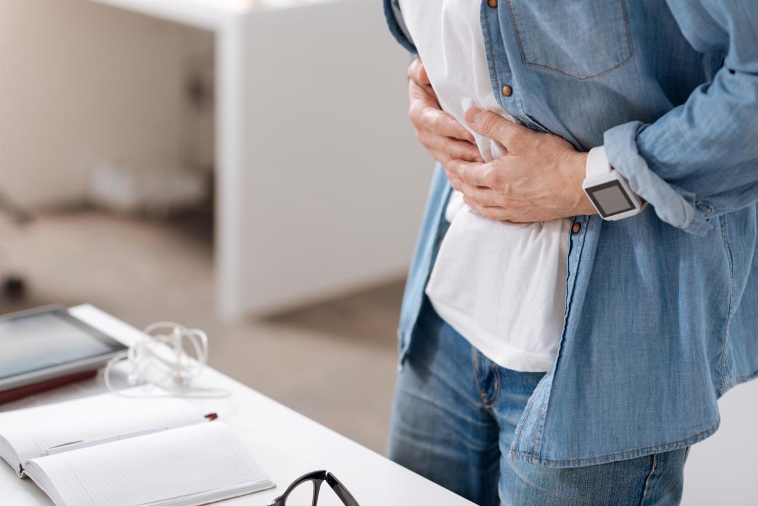 Man with constipation at desk holding his stomach in pain.