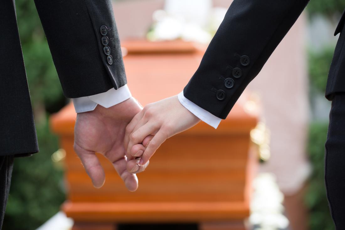 Two people holding hands at a funeral which may be a cause of depression