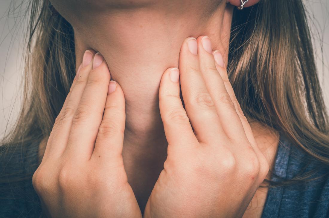 Woman touching sides of neck or throat where thyroid is.