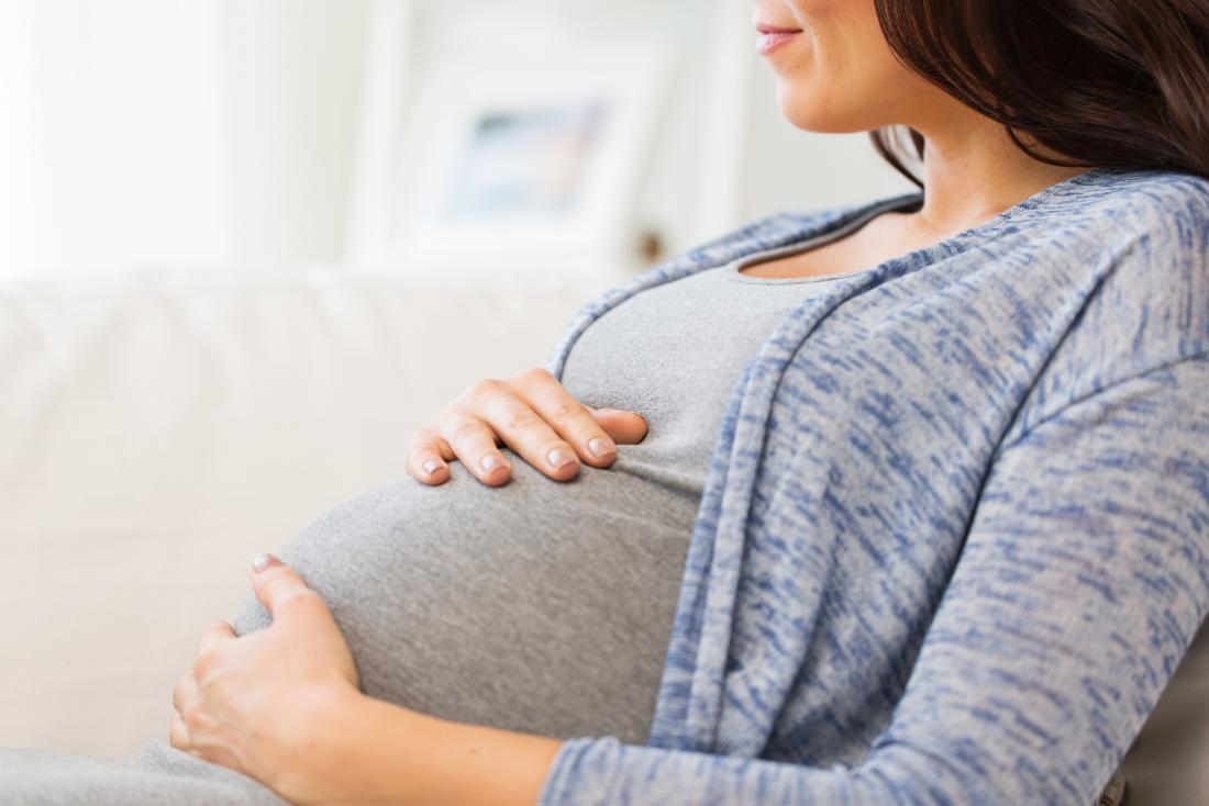 Pregnant woman sitting down and holding her bump.