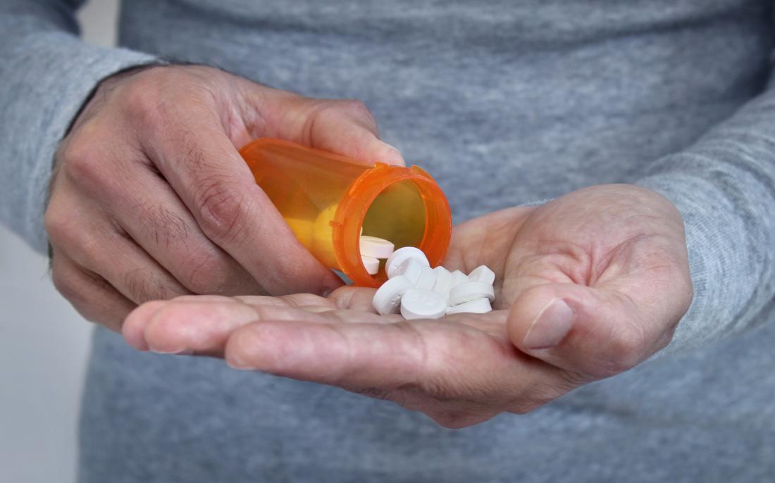 Man pouring pot of pills into palm of hand.
