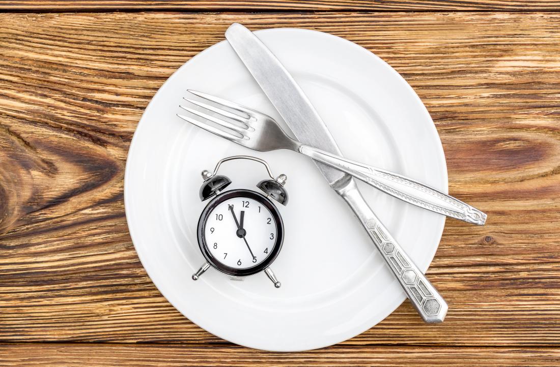 Empty plate on wooden table with knife and fork and alarm clock