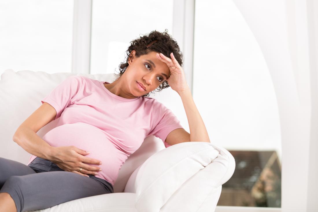 Worried pregnant woman sitting on sofa.