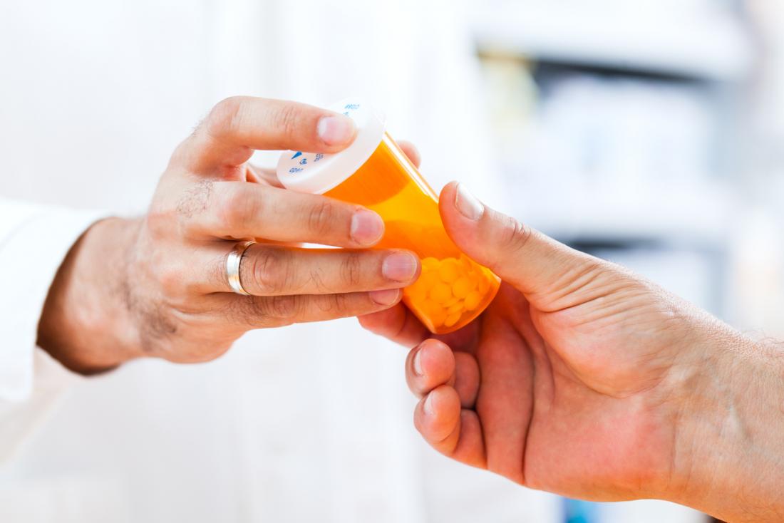 Doctor handing pharmaceutical prescription of drugs or pills in bottle to patient.