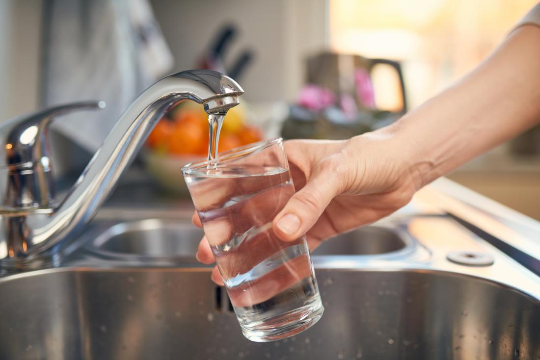 Person pouring water into glass from tap