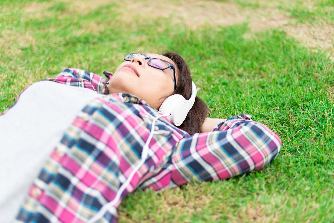 Woman relaxing laying down on grass outdoors listening to music through headphones