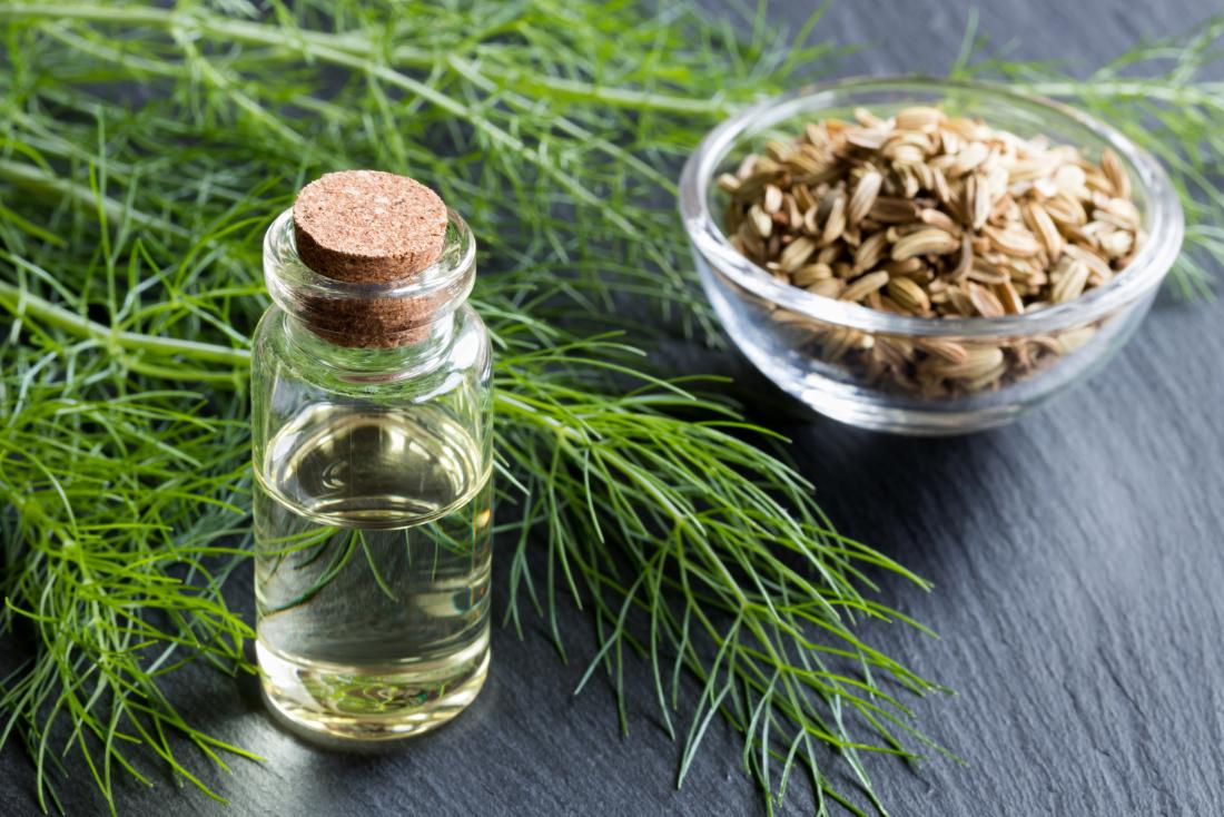 Fennel seeds in bowl next to leaf and bottle of essential oil