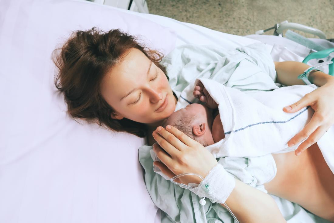 New mother in hospital bed with baby after giving birth.