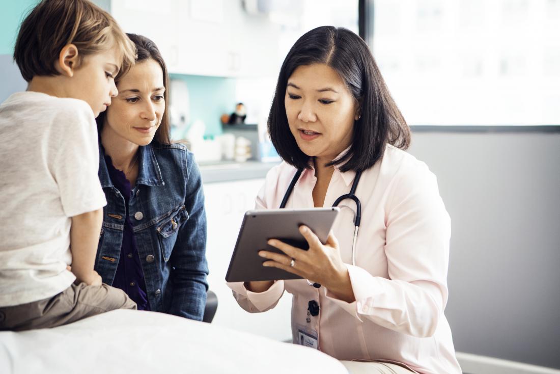 Pediatric doctor showing tablet to parent and child.