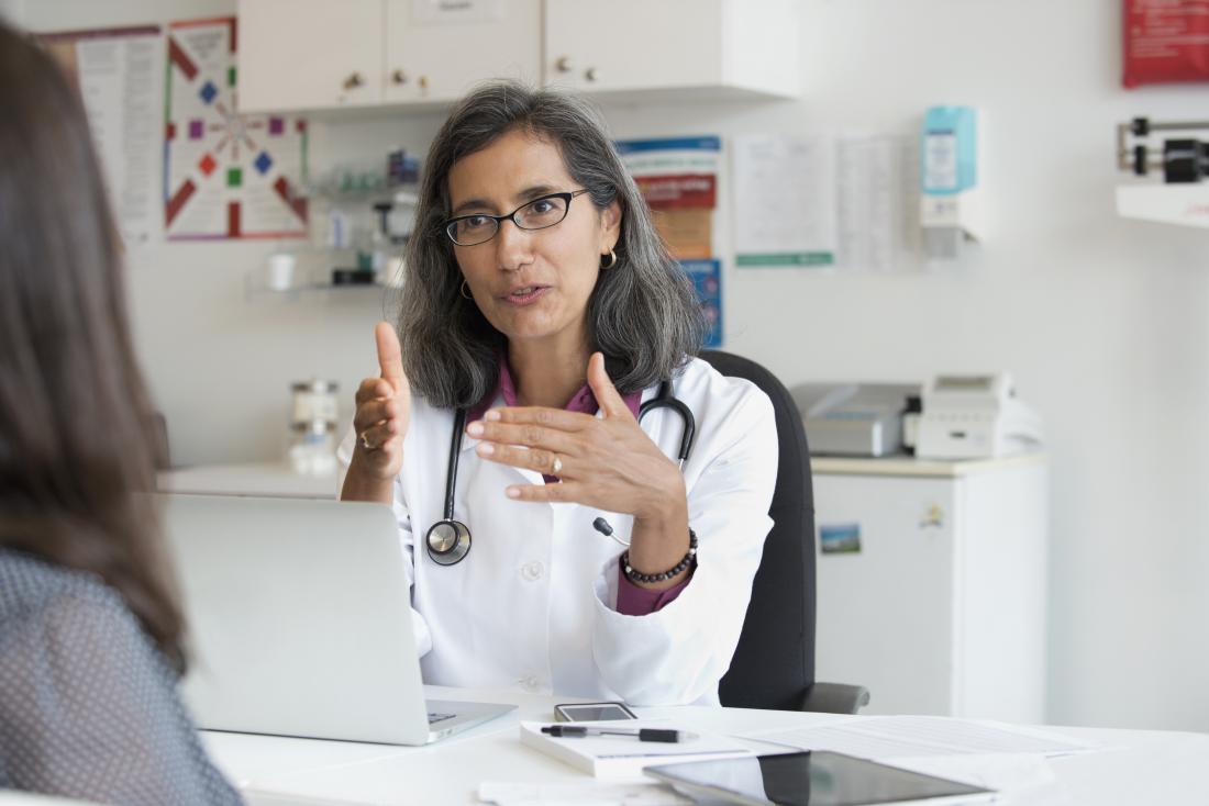 Female doctor in office at desk with laptop explaining something to woman patient.