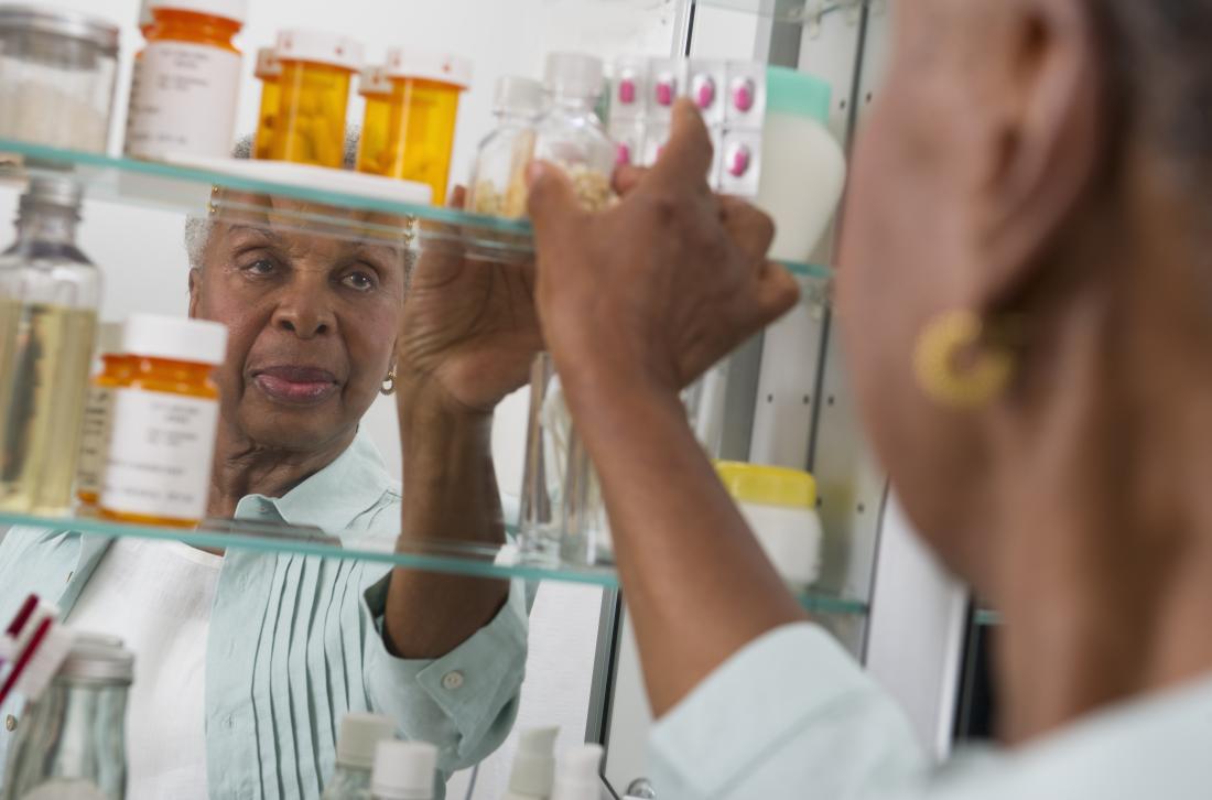 Mature post-menopausal woman reaching for medication in pill bottles in bathroom cabinet.