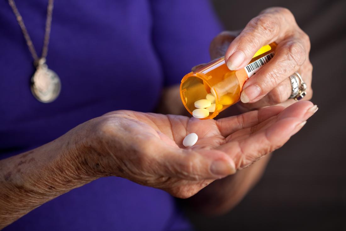 Senior woman pouring pills from medication pot in hand.