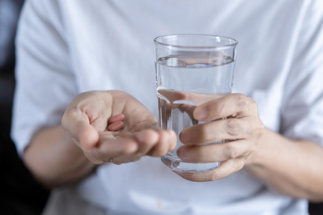person taking painkillers held in palm of hand while holding a glass of water in the other