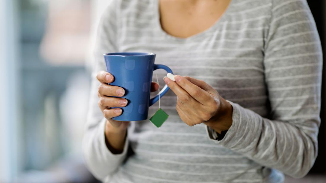 woman holding cup of herbal tea and pill