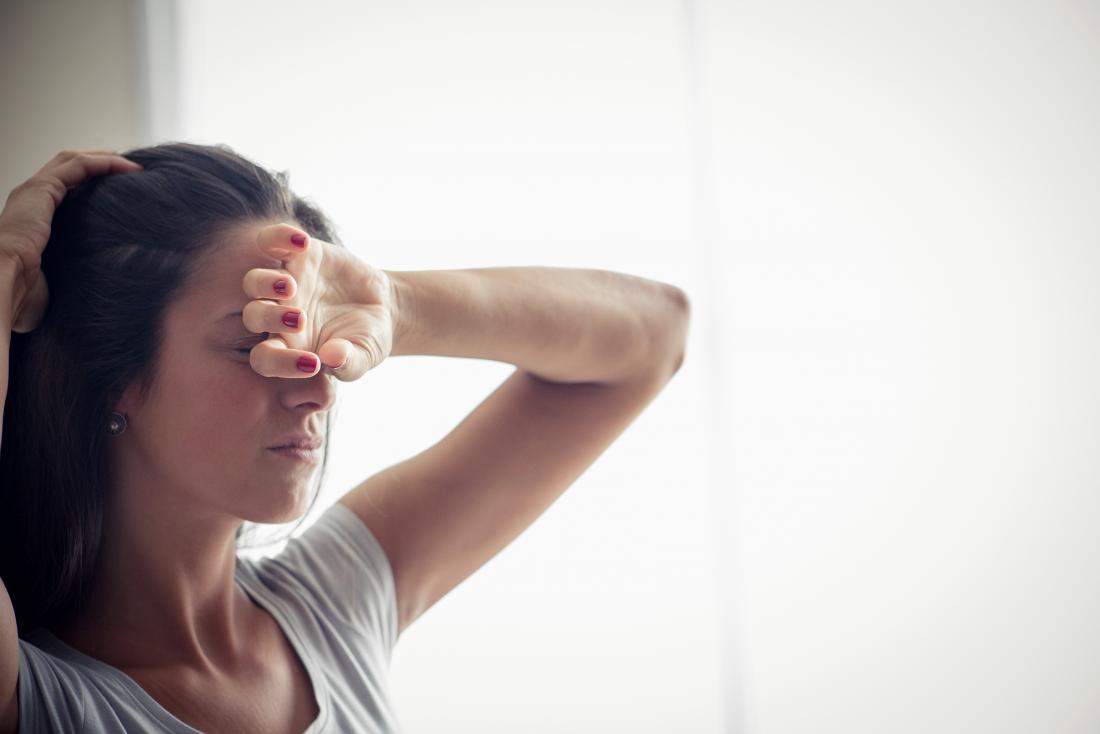 woman with fever and fatigue holding hand to forehead because of temperature//