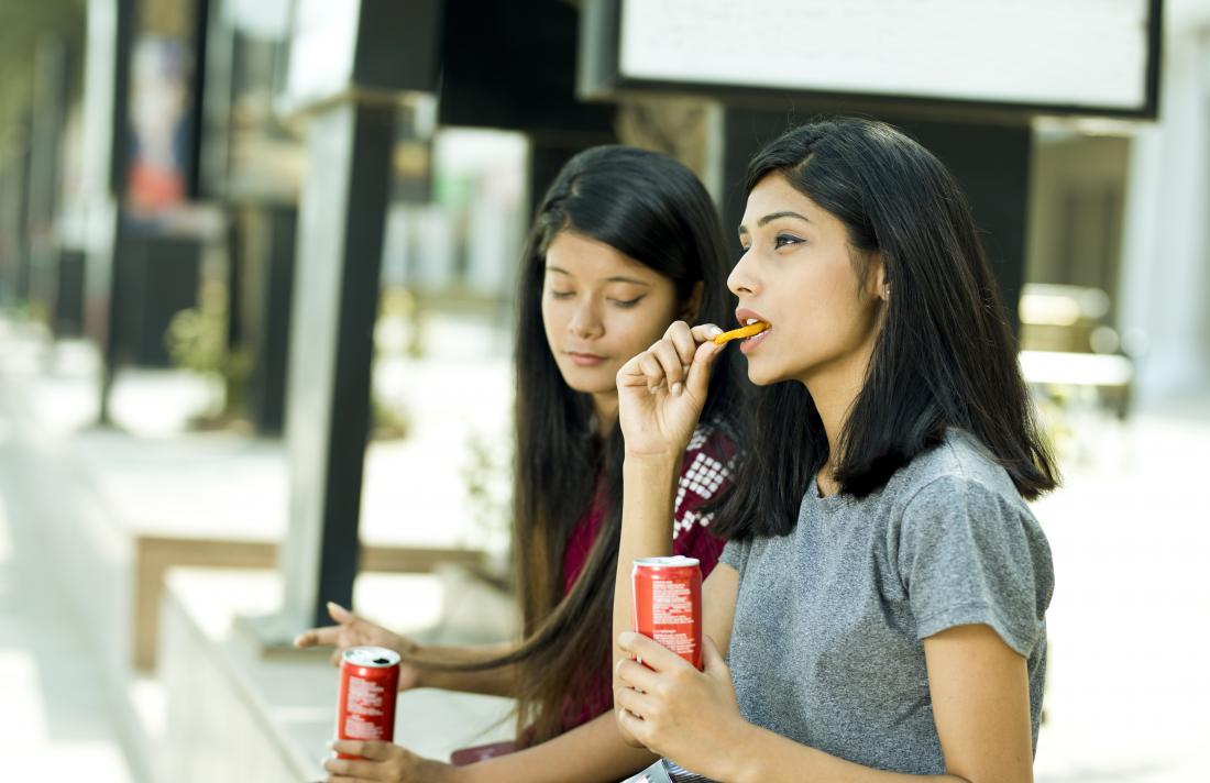 young women drinking soda and eating potato chips