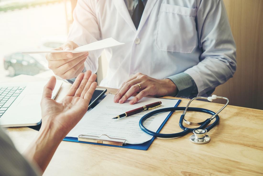 doctor handing prescription over desk to patient