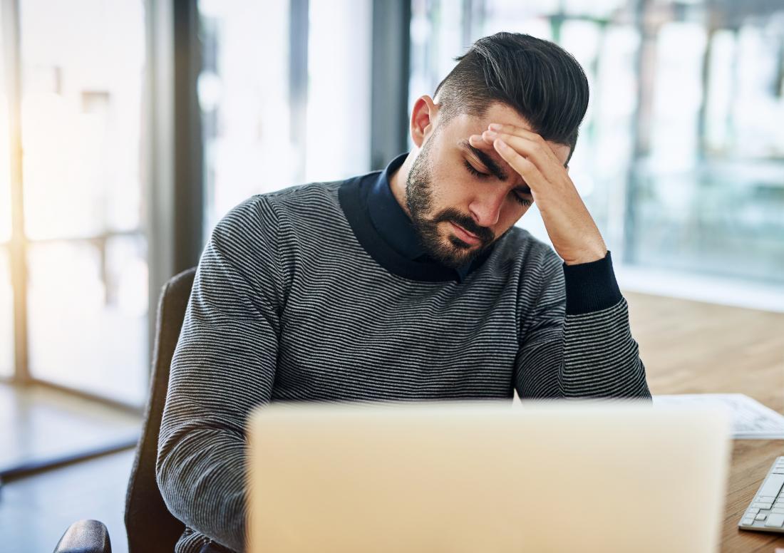 Man working on laptop holding head because of stress
