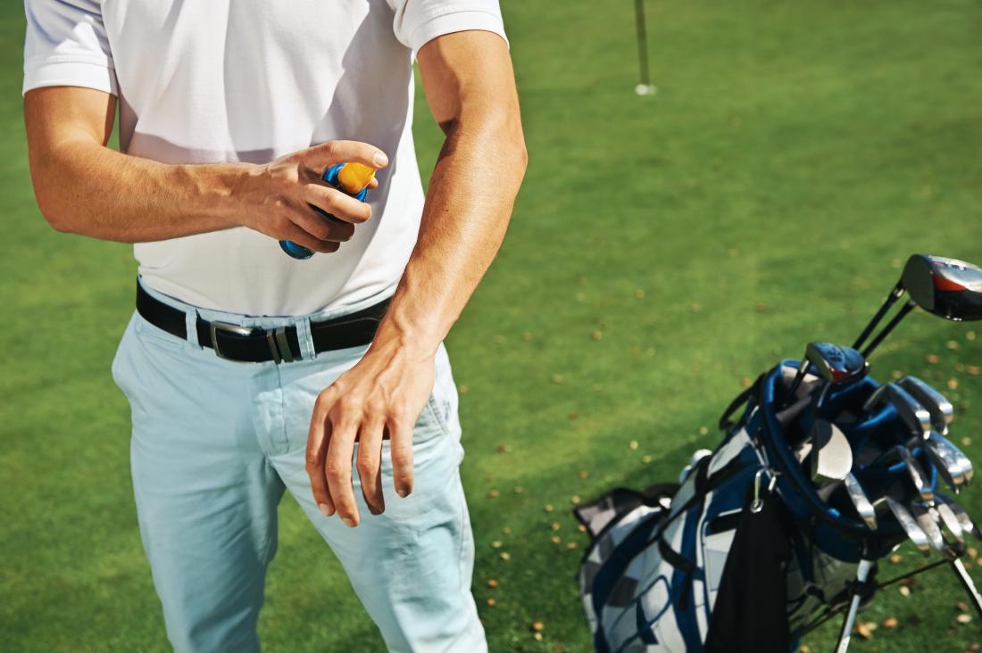 male golfer spraying sun protection on arm