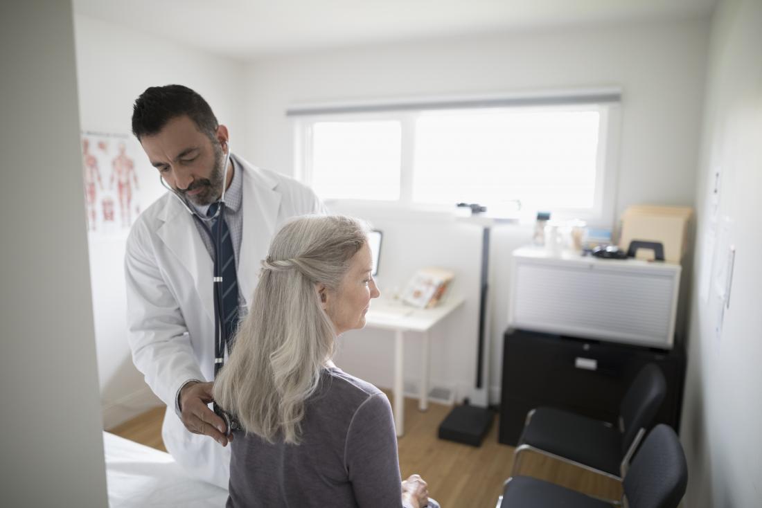 Doctor in clinic listening to patient's breathing using a stethoscope.