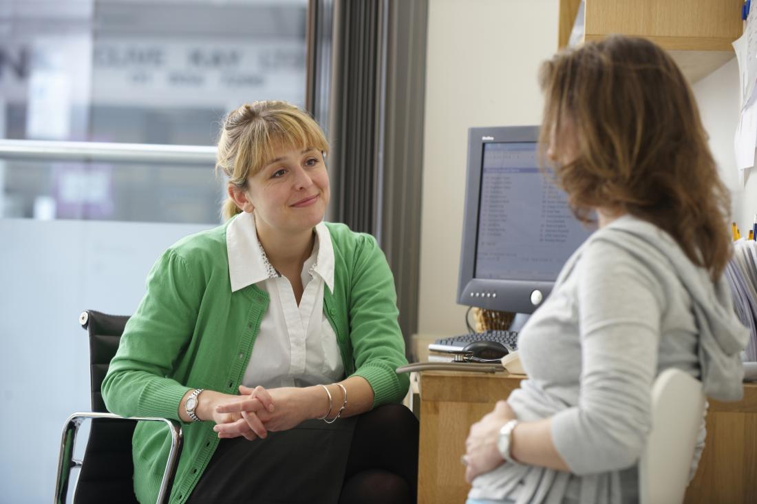 Female patient in early stages of pregnancy speaking to woman doctor in office.