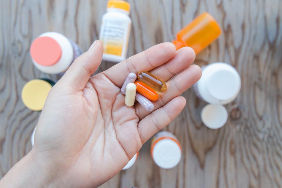 Person holding multiple supplements in palm of hand with bottles below