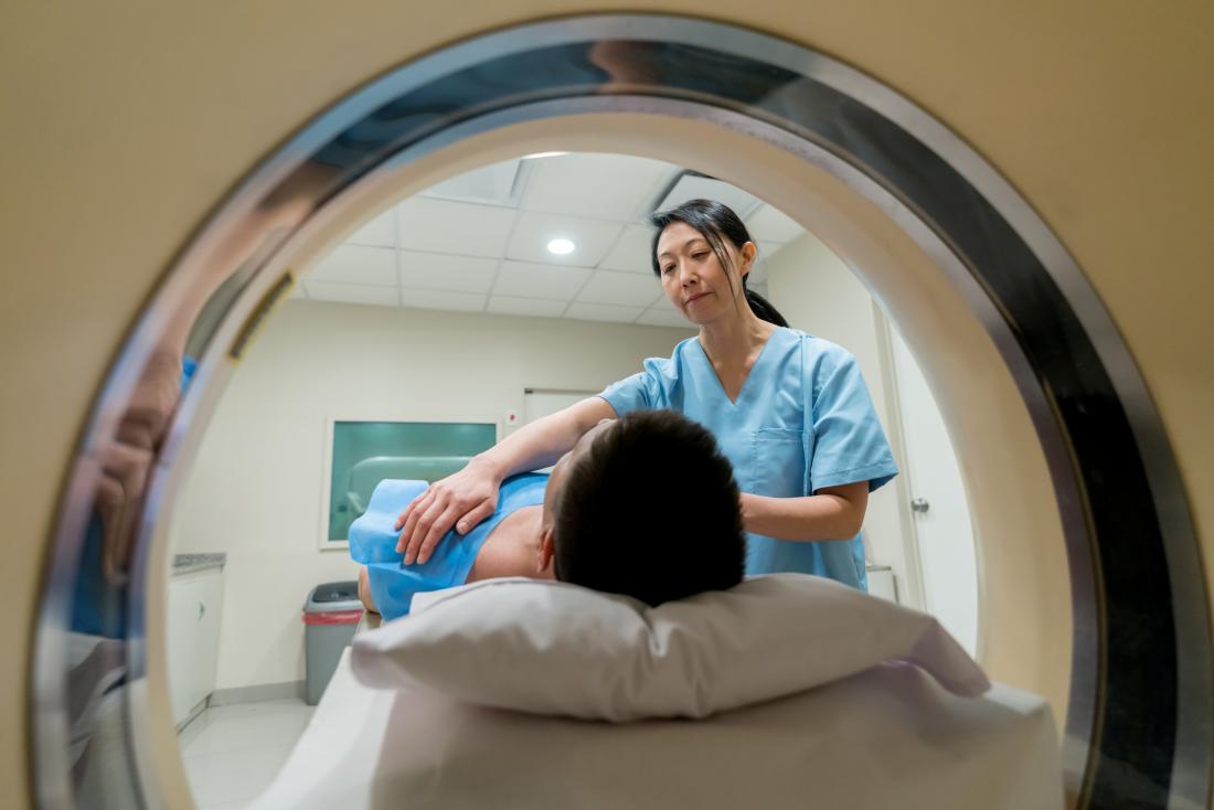 Person having a CT scan going through machine with help of nurse or technician