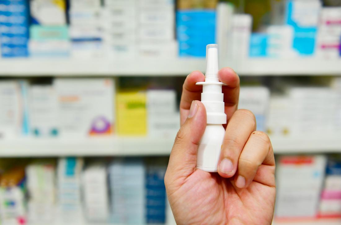 Cromolyn sodium nasal spray being held up by pharmacist in front of shelf of medication