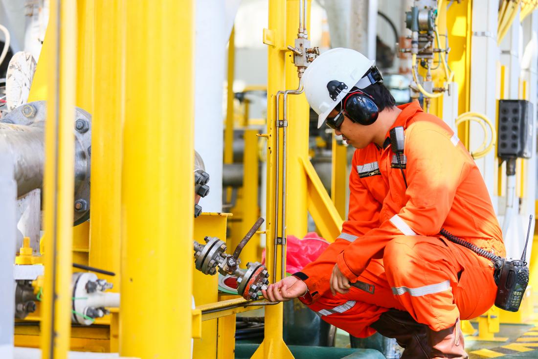 Worker in gas and oil refinery wearing protective gear including noise cancellers and helmet