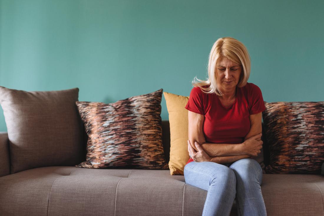 mature lady with stomach ache sitting on sofa