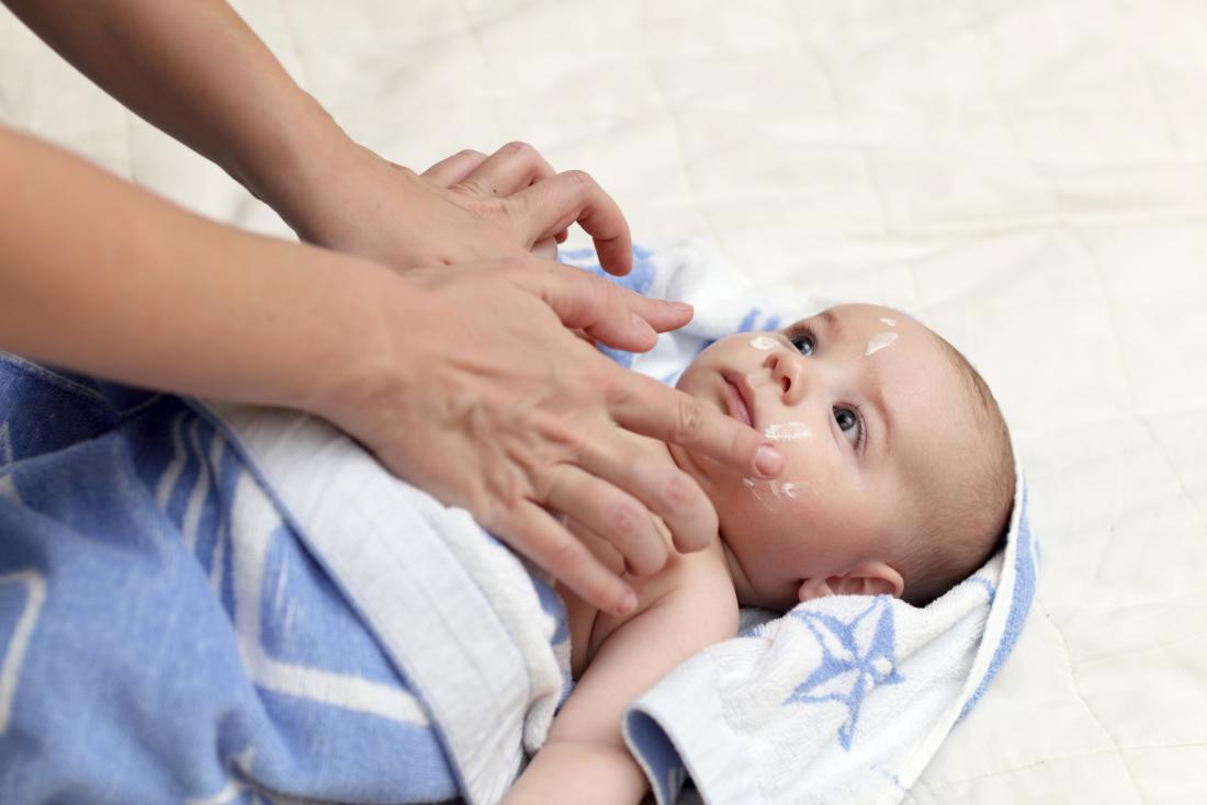 Baby lying down in blanket with woman putting cream on their face