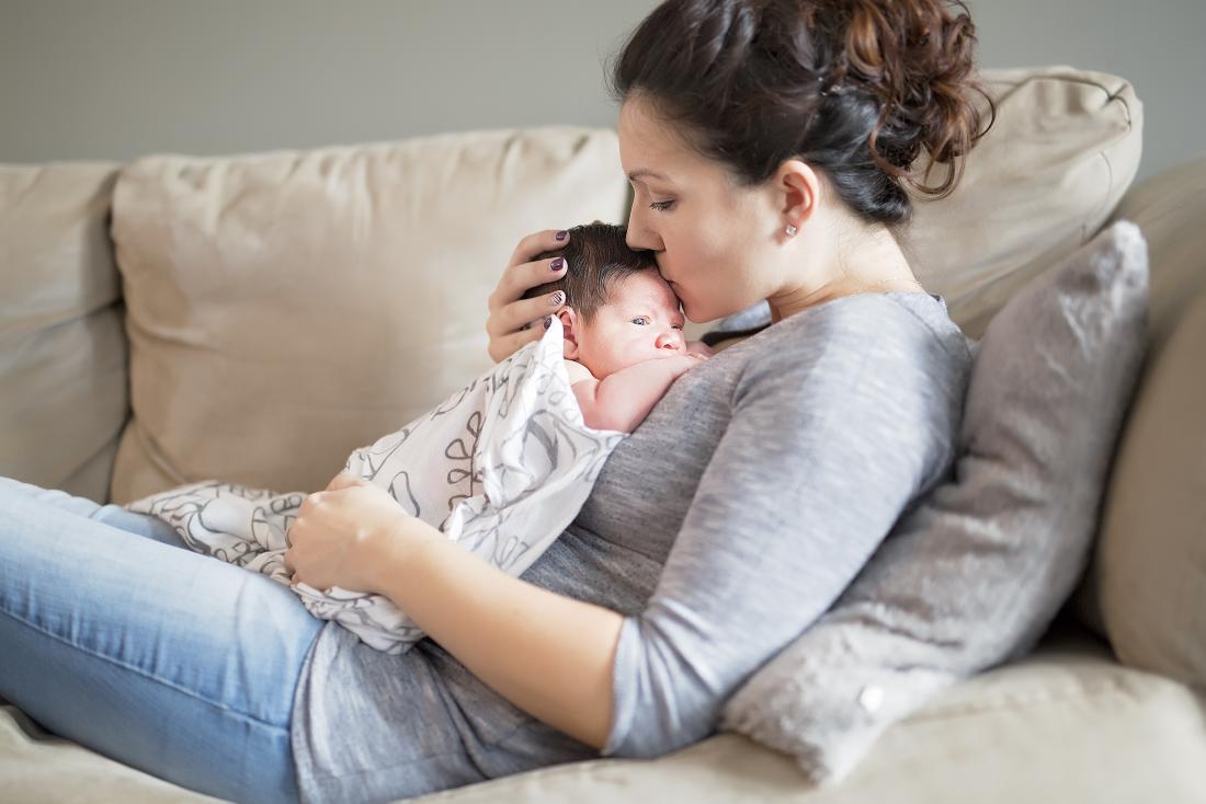 Woman lying on sofa holding baby on chest