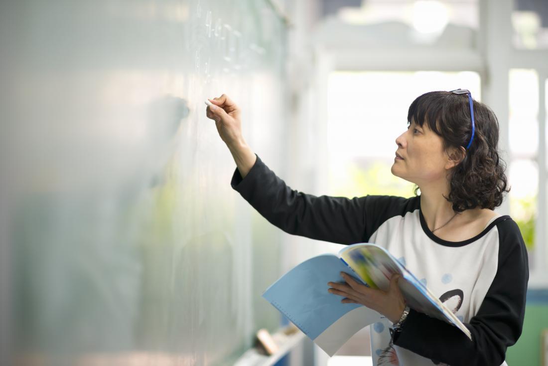 Person reading from book and writing in chalk on board, studying and teaching