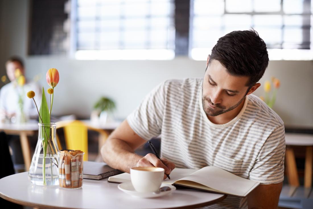 Man writes in a journal in a cafe to keep track of psoriasis and psoriatic arthritis triggers
