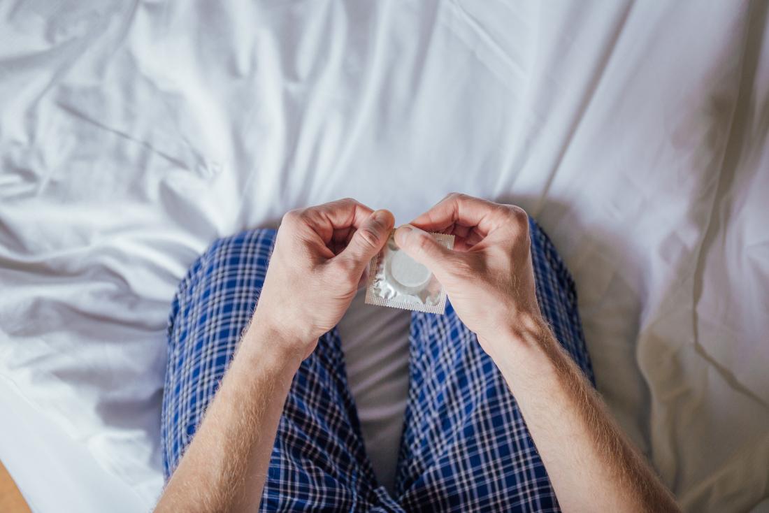 man on bed holding condom in packet