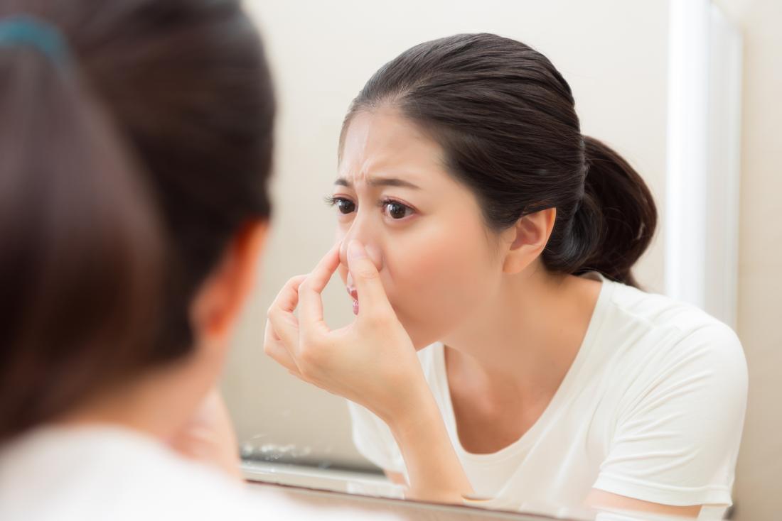Woman inspecting her nose in mirror