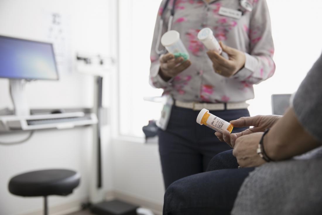 Doctor in office holding different pill bottles discussing prescription medication with patient