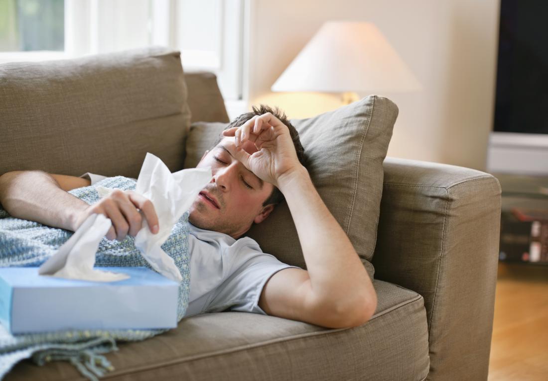 Man lying on sofa grabbing tissues because of cold.