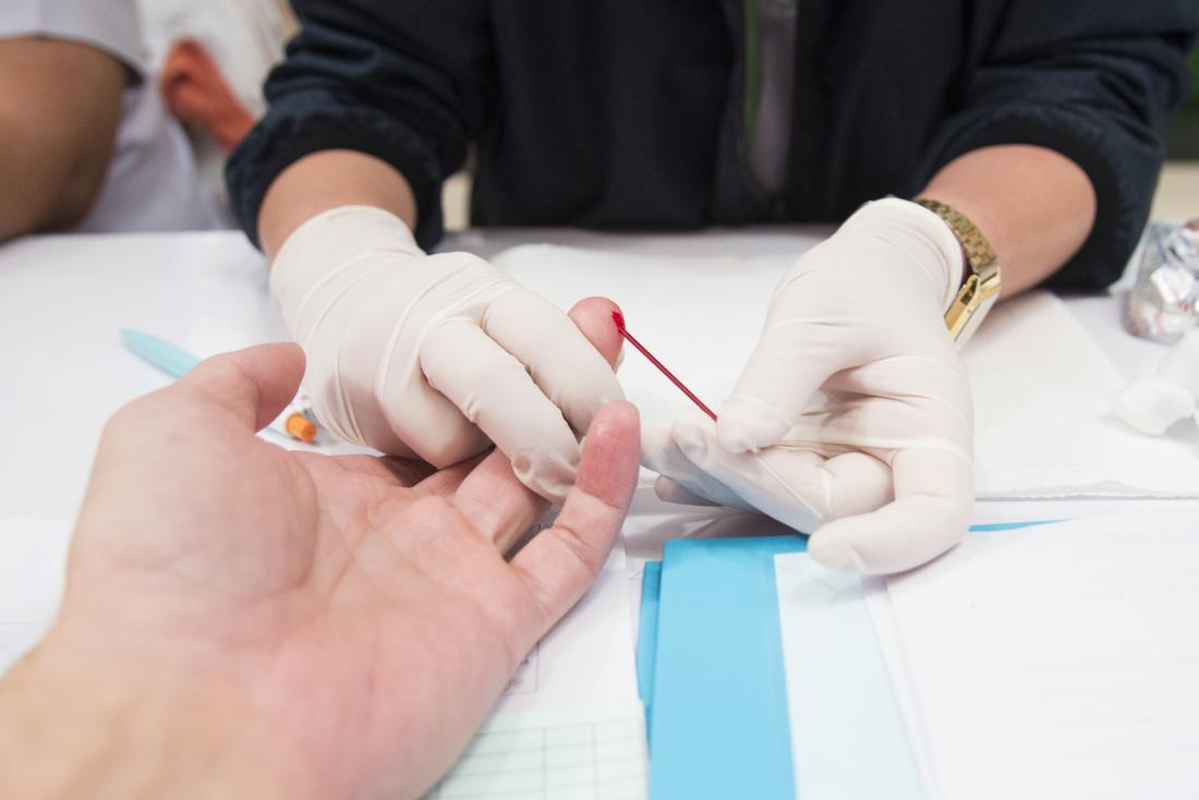 Человек с руками в перчатках берет образец крови из кончика пальца для теста на ВИЧ