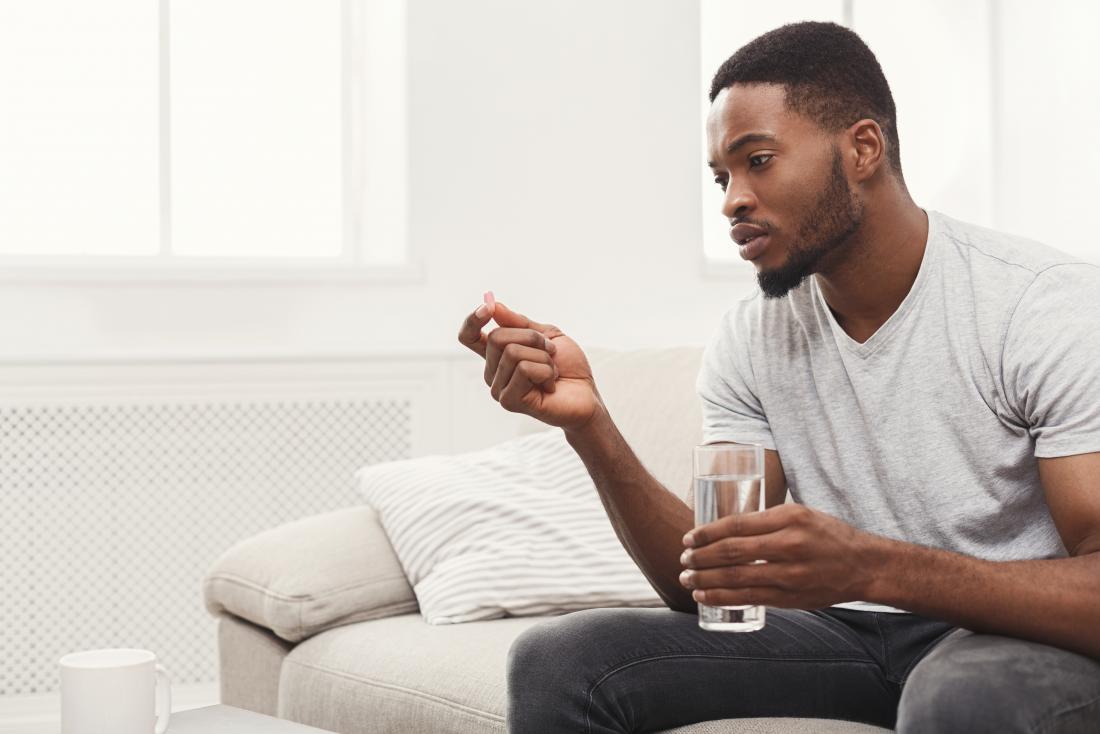 Man holding glass of water and pill taking medication.